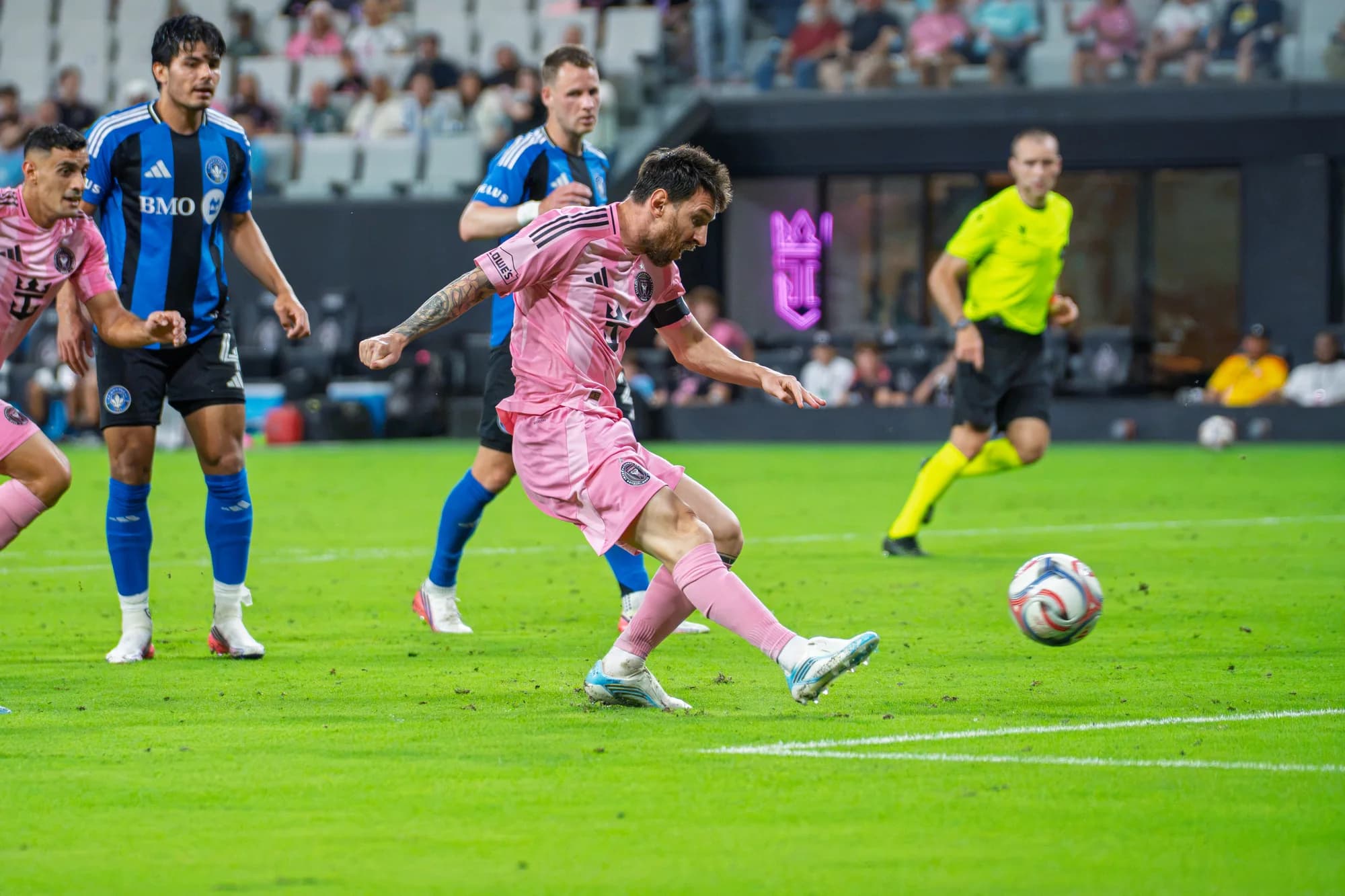 A pink-shirted player striking the ball with opponents and a referee in the background