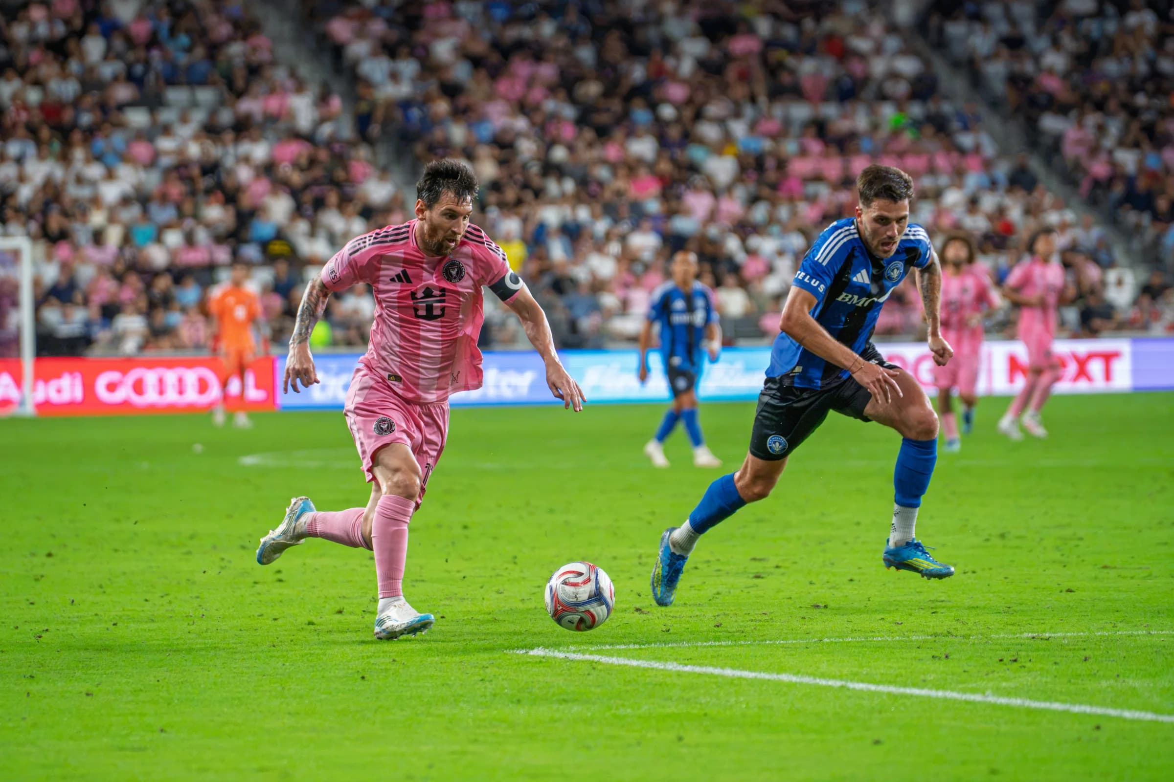 Two soccer players in pink and blue-and-black kits racing toward the ball during a match