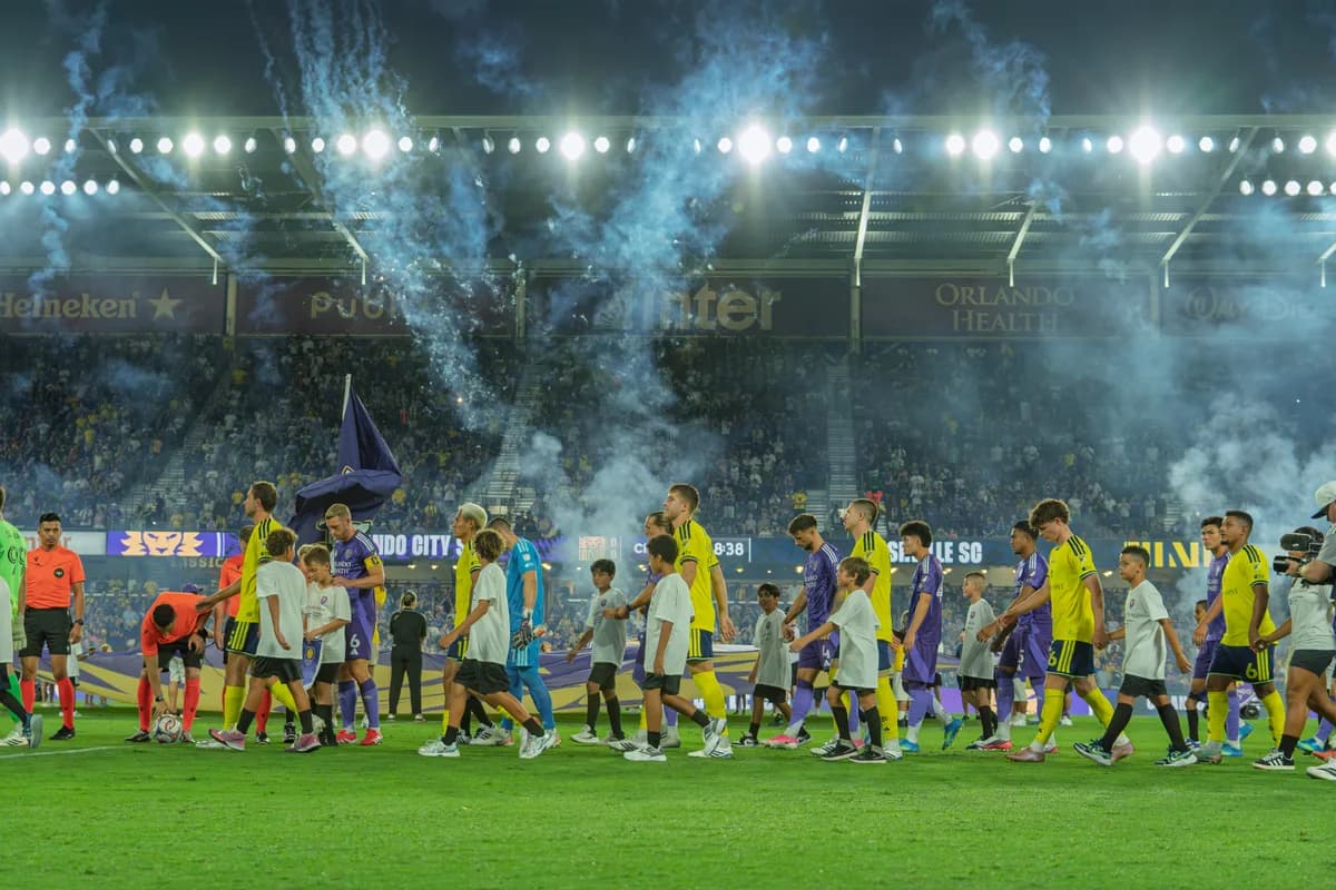 Players and children walking onto the pitch beneath stadium lights and drifting smoke